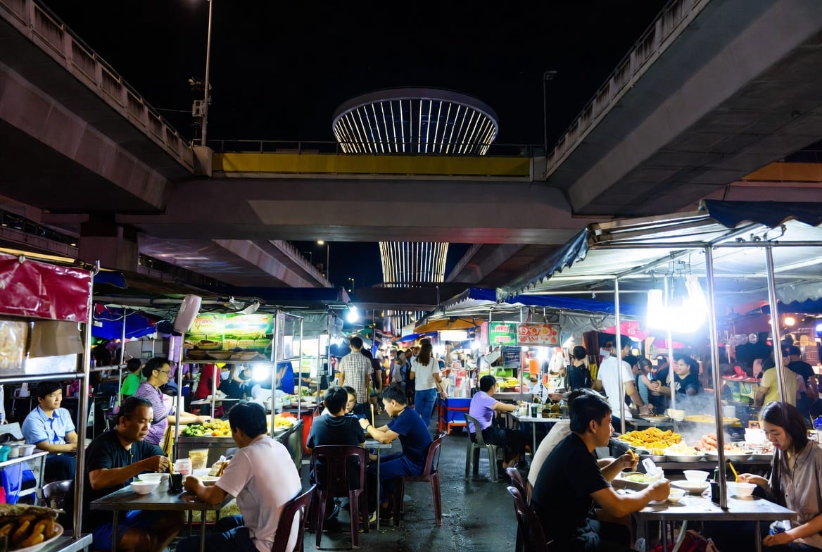 Food stalls and diners beneath the elevated roads near Victory Monument at night