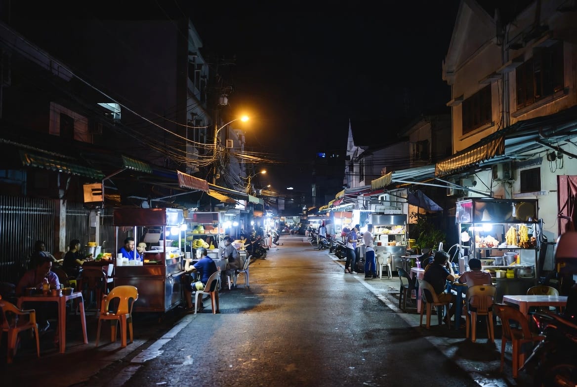 A quiet residential street in Thonburi lined with evening food stalls