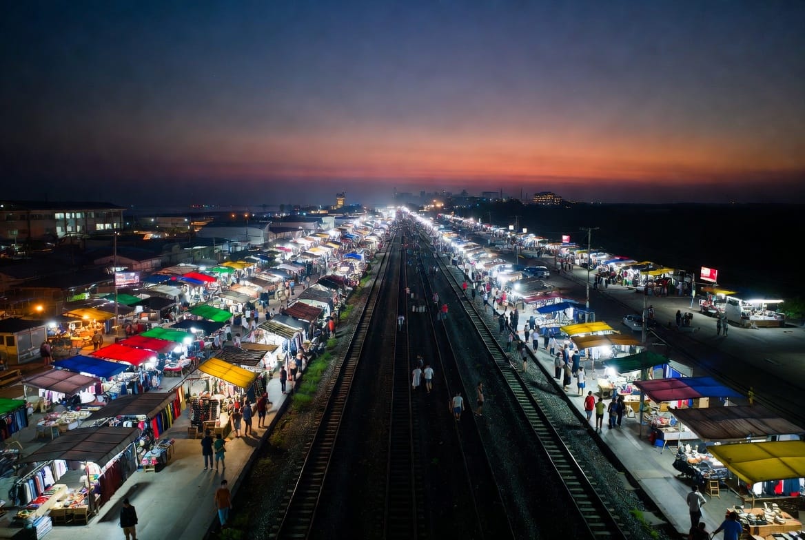 Market stalls glowing at dusk beside the railway tracks at Talat Phlu