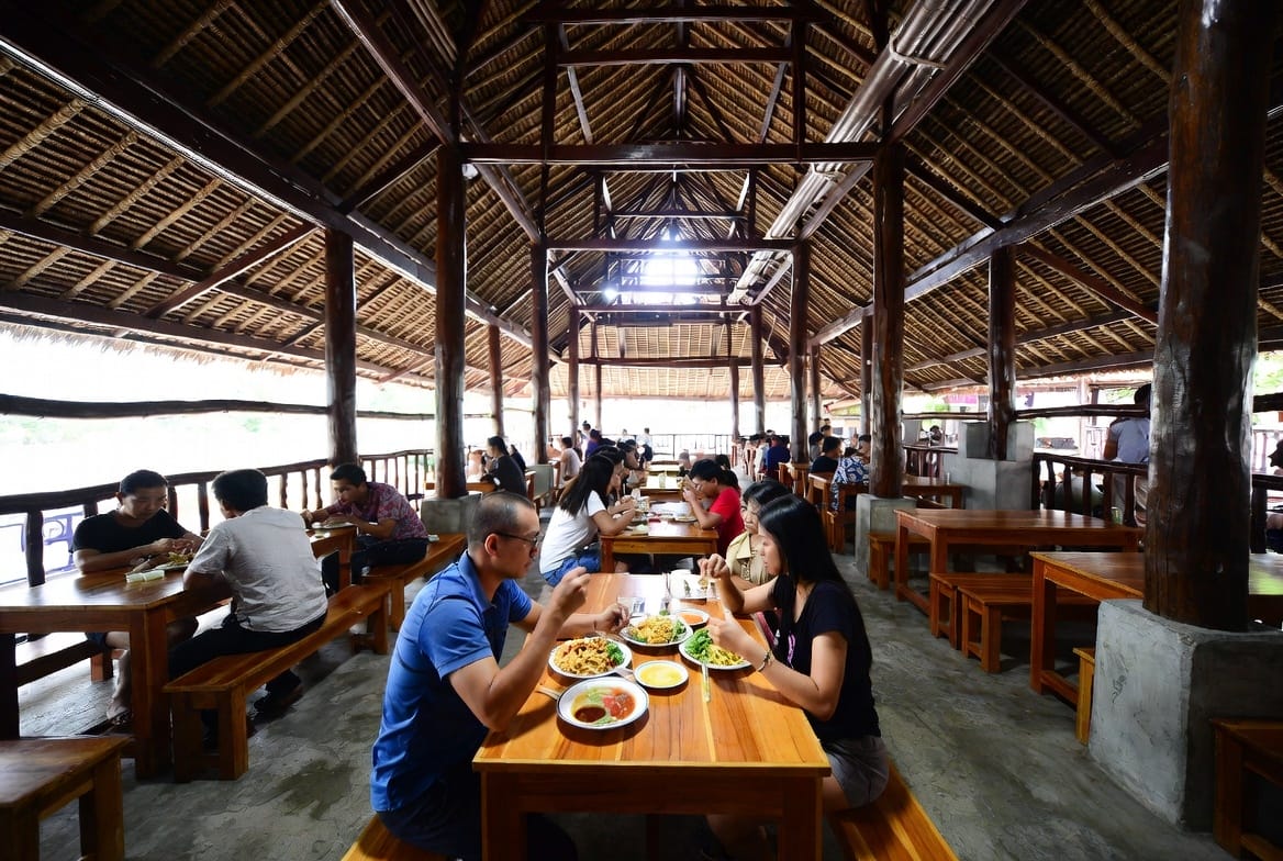 Diners at wooden tables in the traditional open-air food court of Nang Loeng market
