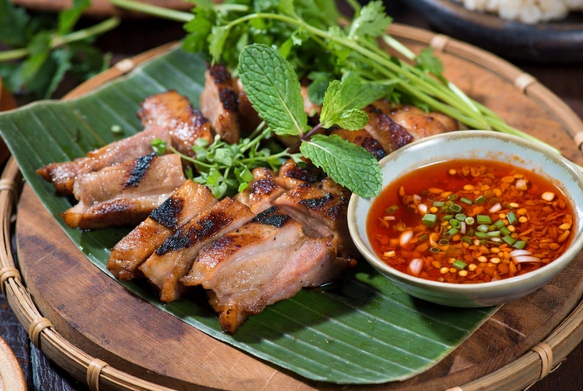 Grilled pork neck sizzling over charcoal at an Isan stall