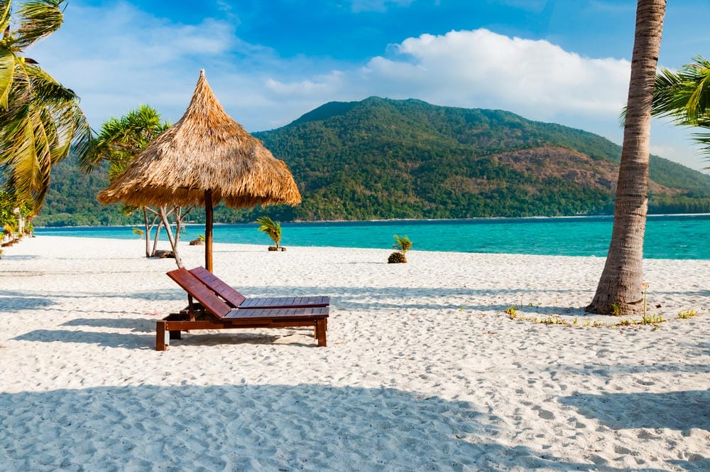 A quiet white-sand Thai beach with a lounge chair and palm trees