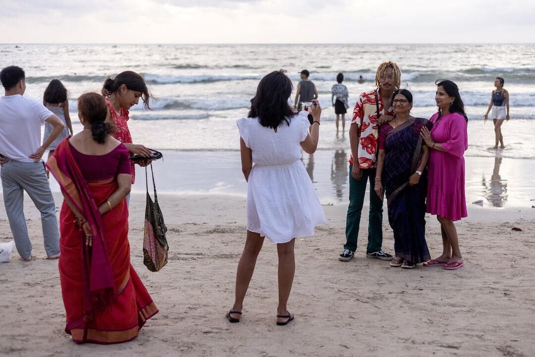 Indian families in saris and holiday clothes posing for photographs on a Thai beach at dusk